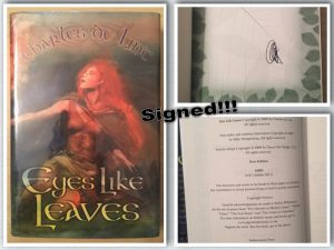 Three photos: first is of book cover with Charles de Lint's name curved across the top in a blueish font, and the title _Eyes Like Leaves_ in yellow across the bottom. Image is of a red-haired girl in cloak and fairy-type garb. Top right image is paper with green leaves on the edge, and what looks like a scrawl, but is actually Charles de Lint's signature. Bottom right has the copyright information & says First Edition.