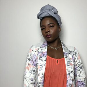 Morgan Greene of Is Was Will Be wearing gray headwrap, floral blazer, and orange camisole